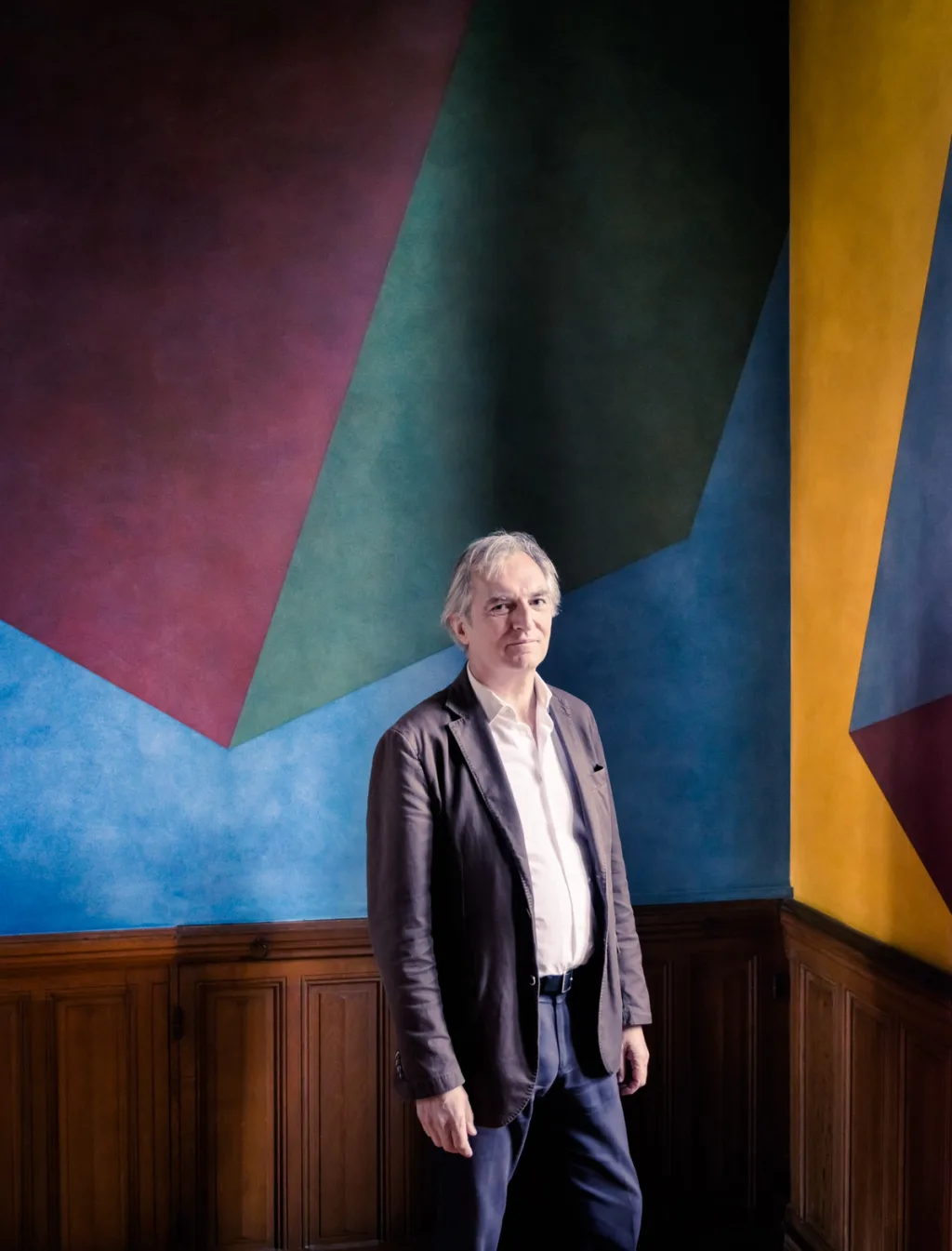 Man standing in front of a large multicoloured geometric wall painting at Donjon de Vez