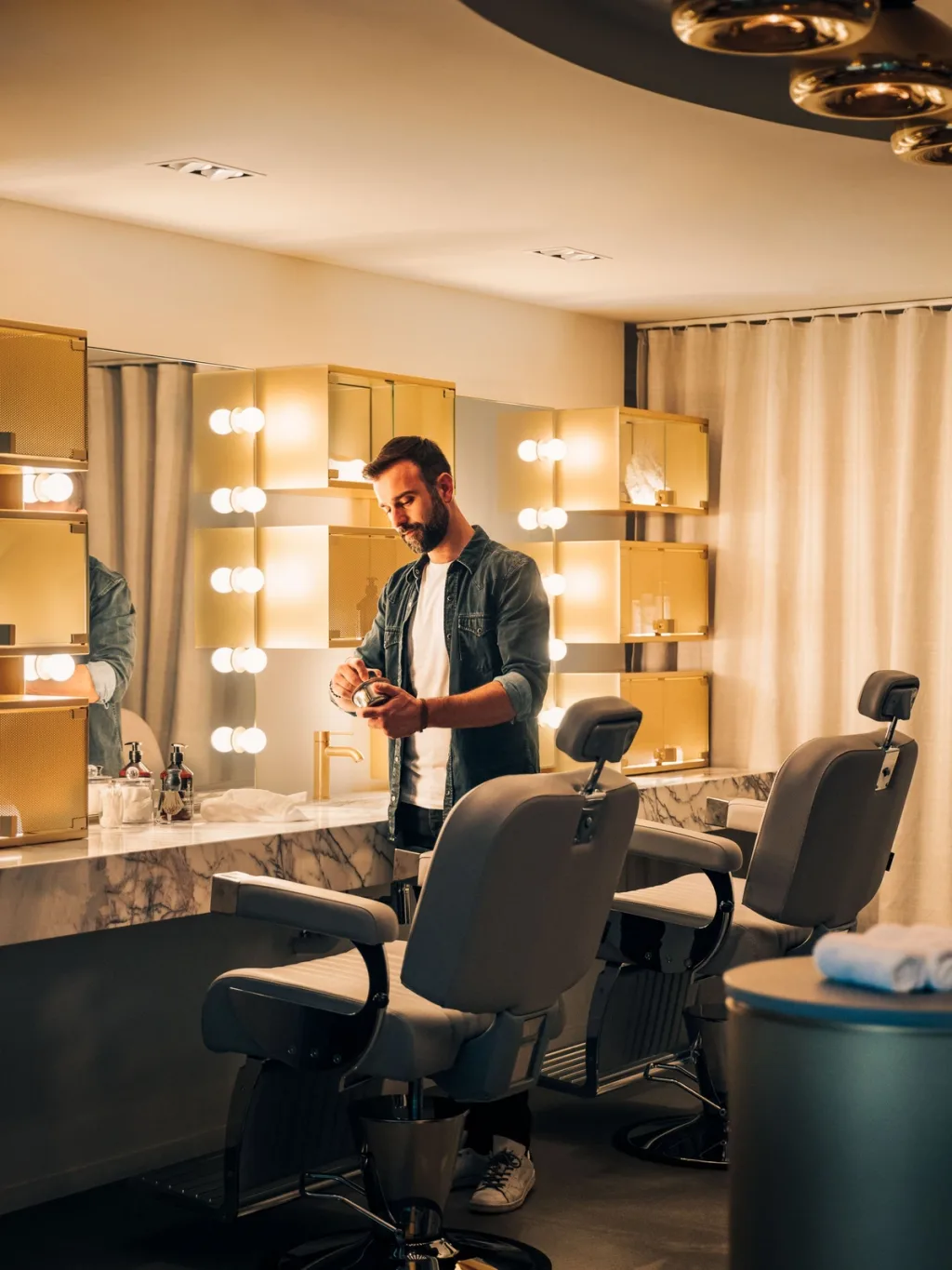 Barber mixing pomade at a gold-lit vanity between leather chairs, Pullman Bercy hotel