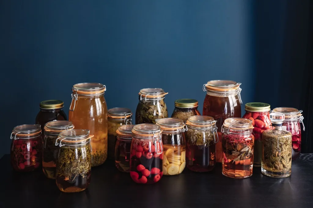 Glass jars of preserved fruit and herbs on a dark table for Cyril Lignac’s Saisons cookbook