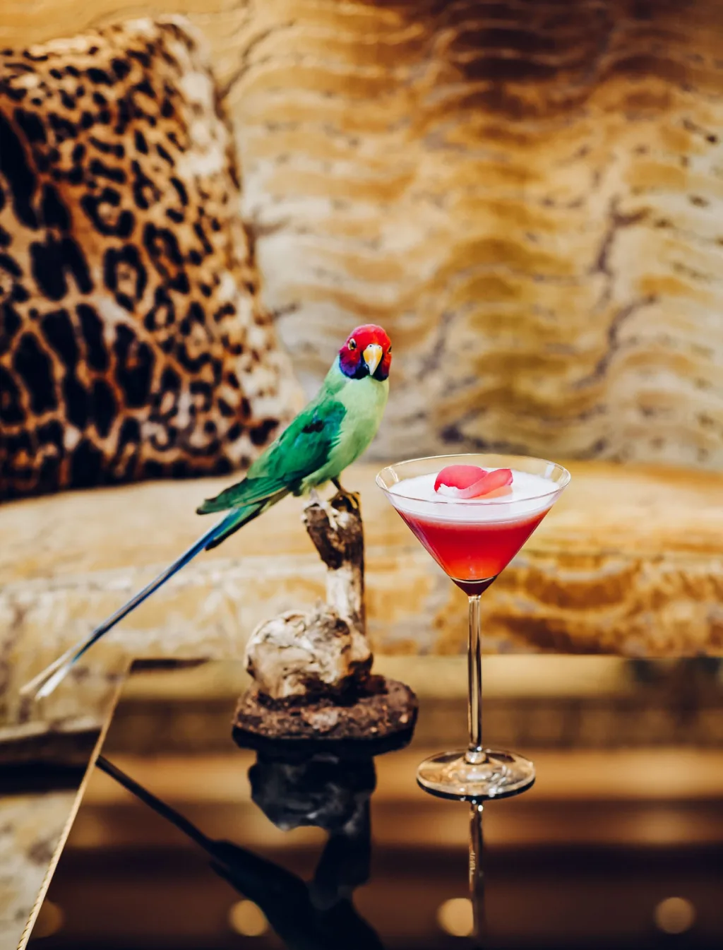 Pink-topped cocktail beside a green bird ornament and animal-print cushions at Hôtel Bristol