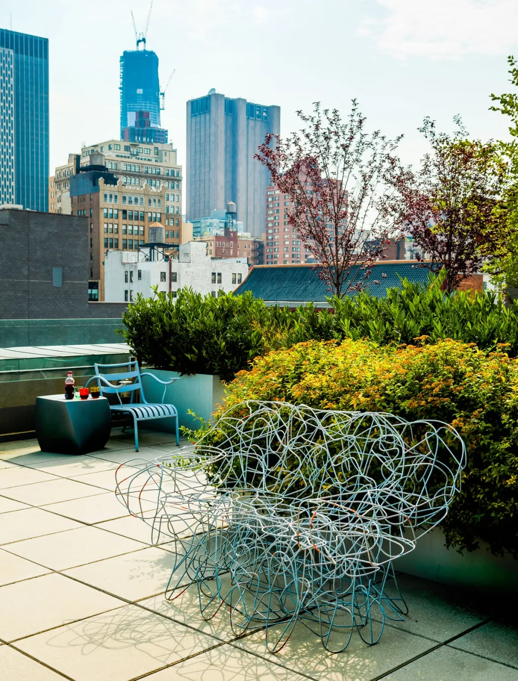 Wire lounge chair among rooftop shrubs with a city skyline beyond, Suzanne Slesin, New York
