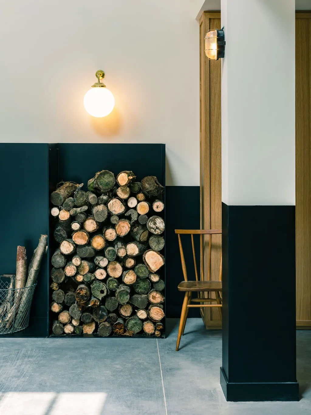 Stacked firewood in a wall rack lit by a brass globe sconce, Le Barn hotel