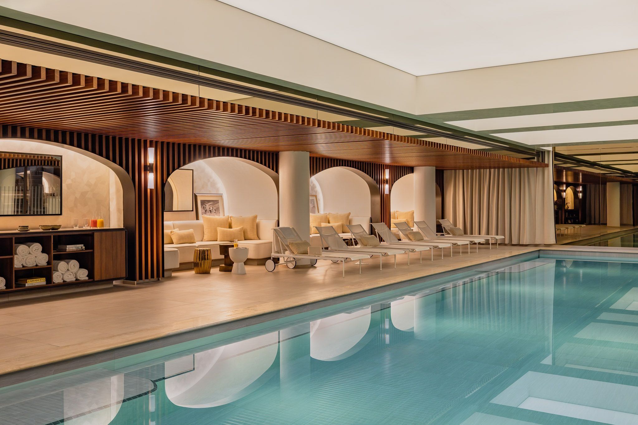 Indoor pool at Hôtel d’Aubusson, with loungers along the water and curved seating alcoves beneath a slatted wood ceiling.