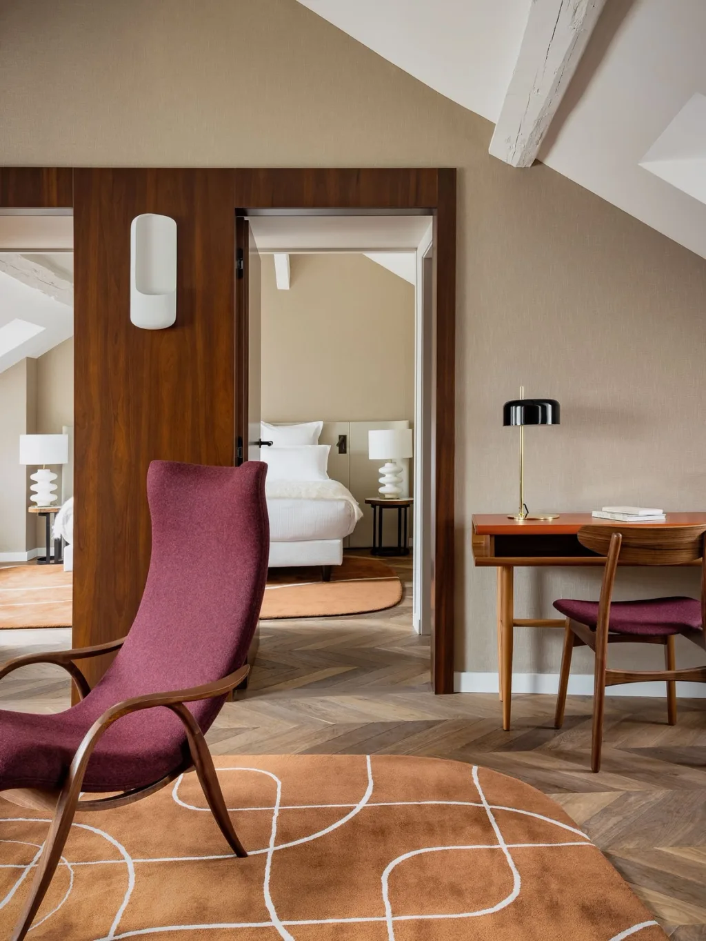 Suite with a burgundy lounge chair and bedroom visible through a wood-framed door at Hotel Pavillon St Germain, Paris