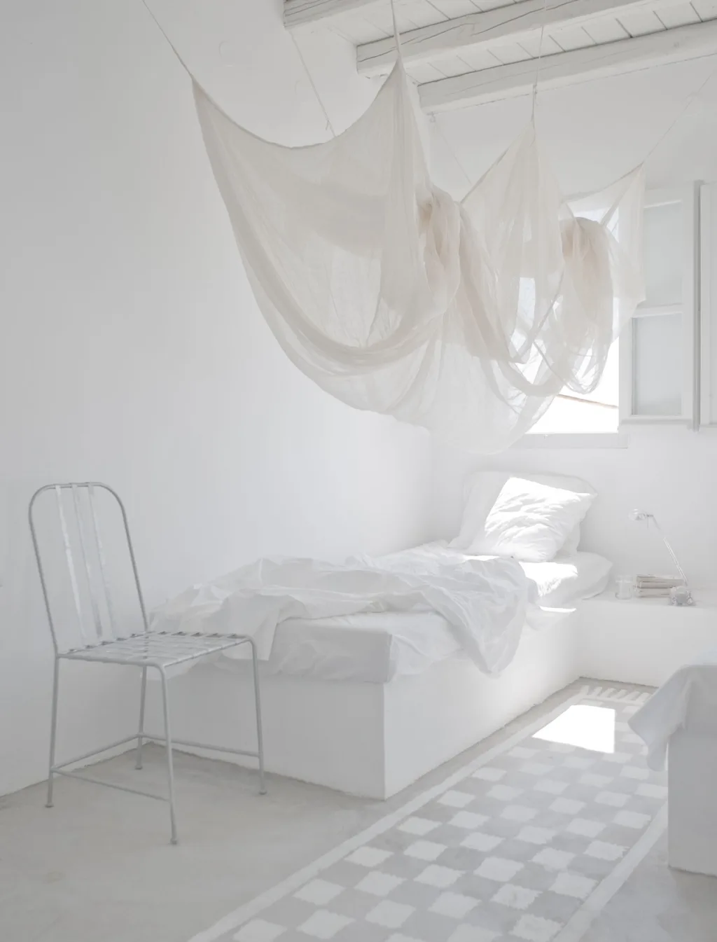 Narrow white bedroom with suspended drapery and a painted checkerboard floor, Paola Navone, Serifos