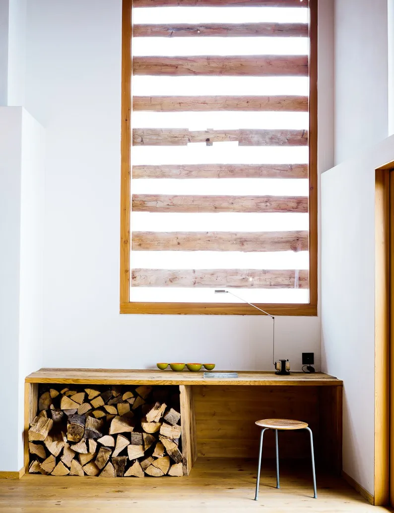 Wood bench with firewood storage beneath a slatted window at Montagne Alternative hotel, Switzerland