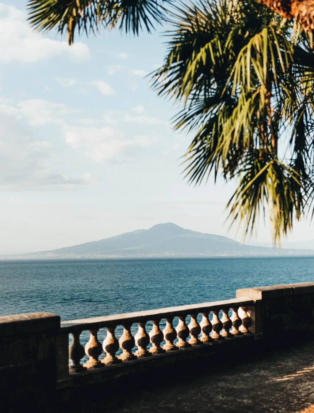 Sea and distant mountain seen past a balustrade beneath palm fronds at Villa Astor