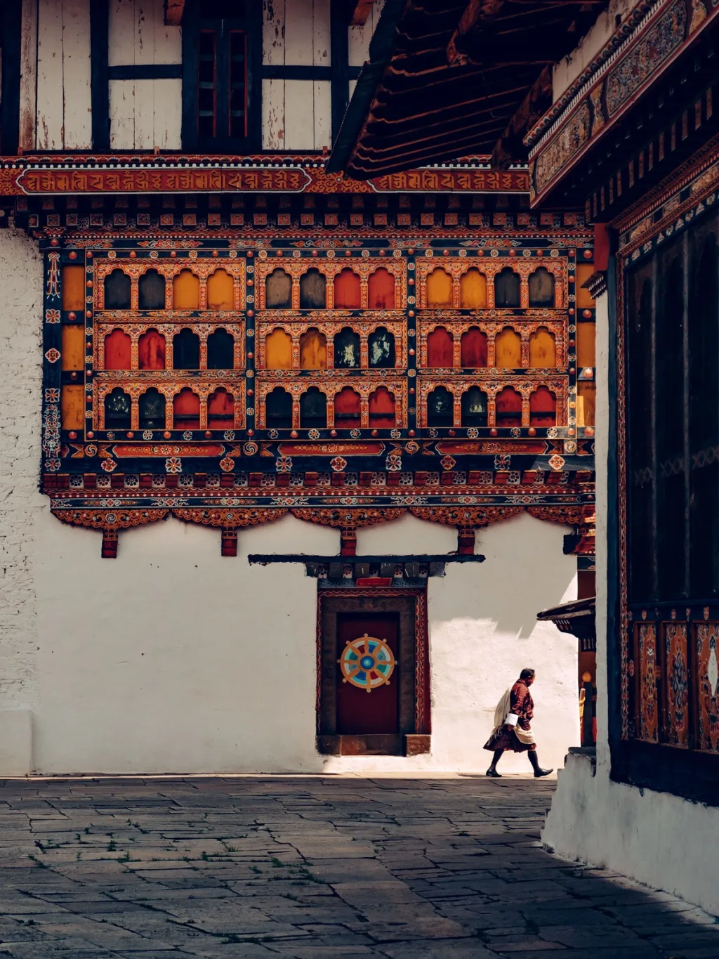 A monk walking through a courtyard of a painted Bhutanese monastery, photographed for Six Senses Bhutan hotel