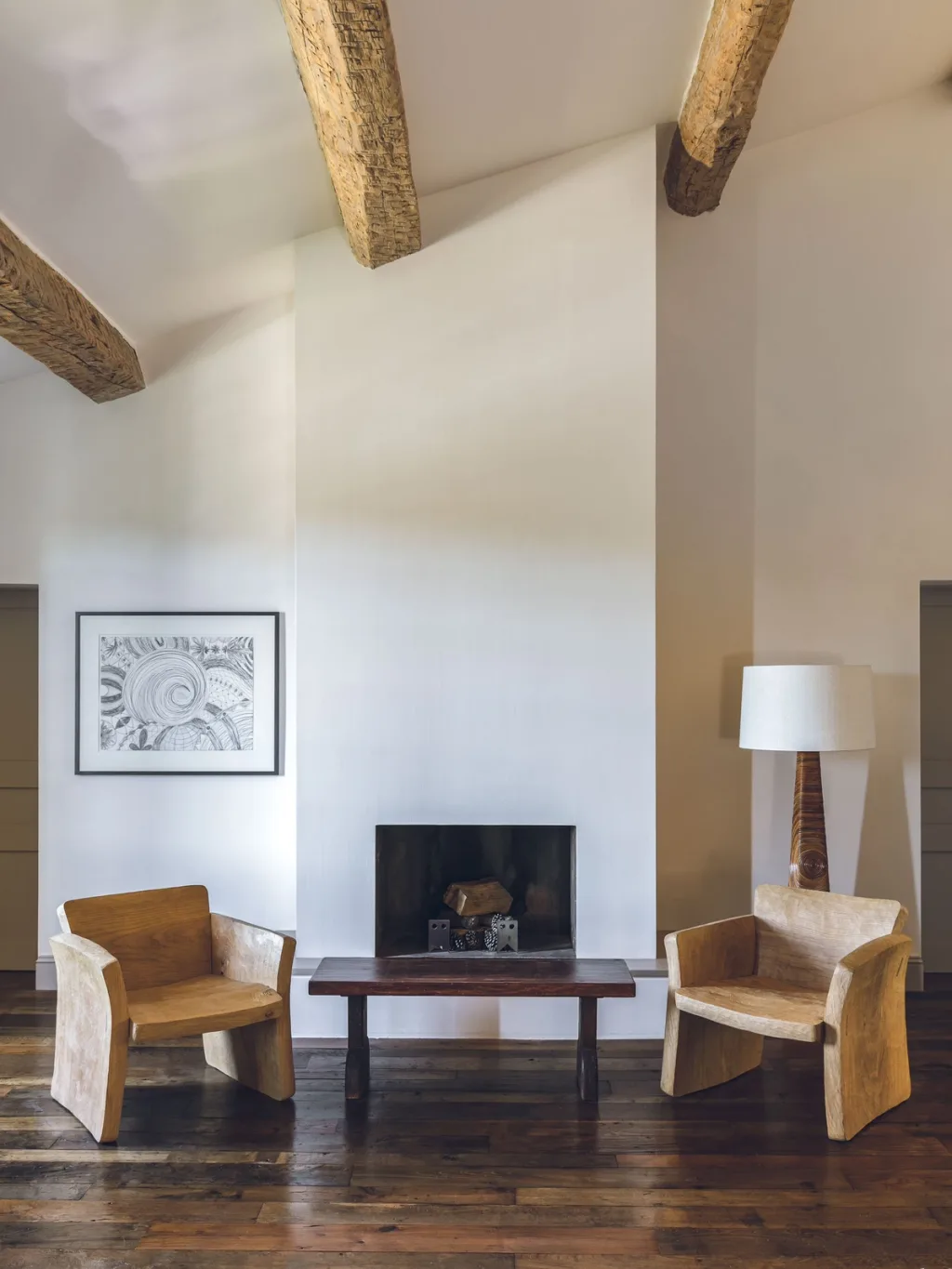 Two angular wooden armchairs beside a tall white fireplace at Fabrègues, Pierre Yovanovitch