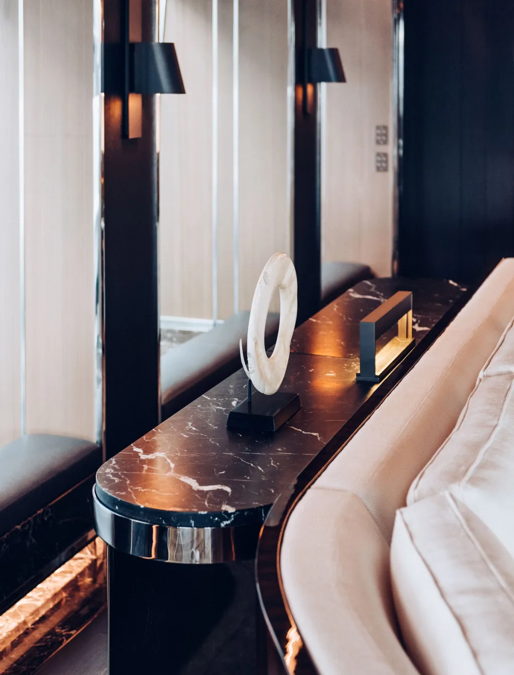 Ring-shaped sculpture on a narrow veined console behind a white sofa aboard Atlante