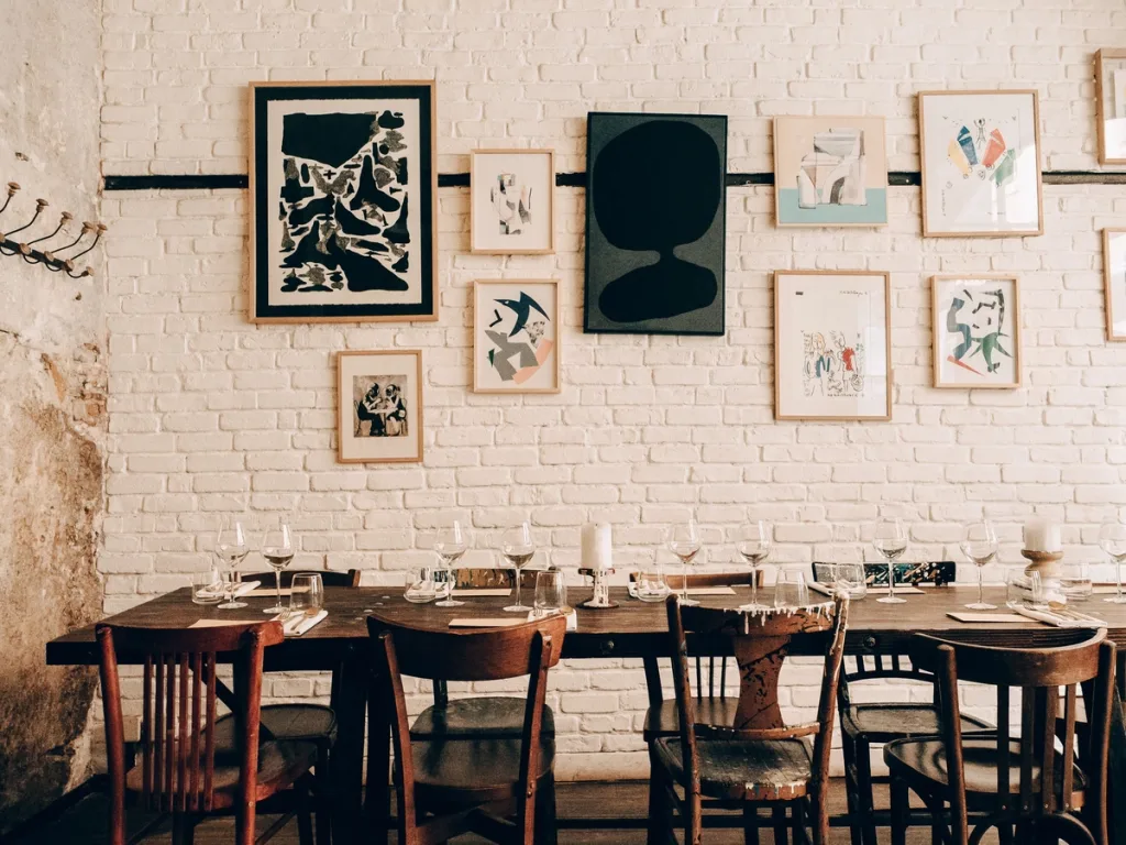 Mismatched wooden dining chairs beneath framed art on a white brick wall in a Lyon restaurant
