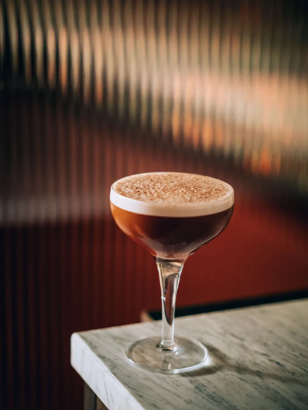 Dark cocktail with a thick foam cap beside ribbed glass for Cyril Lignac’s Saisons cookbook