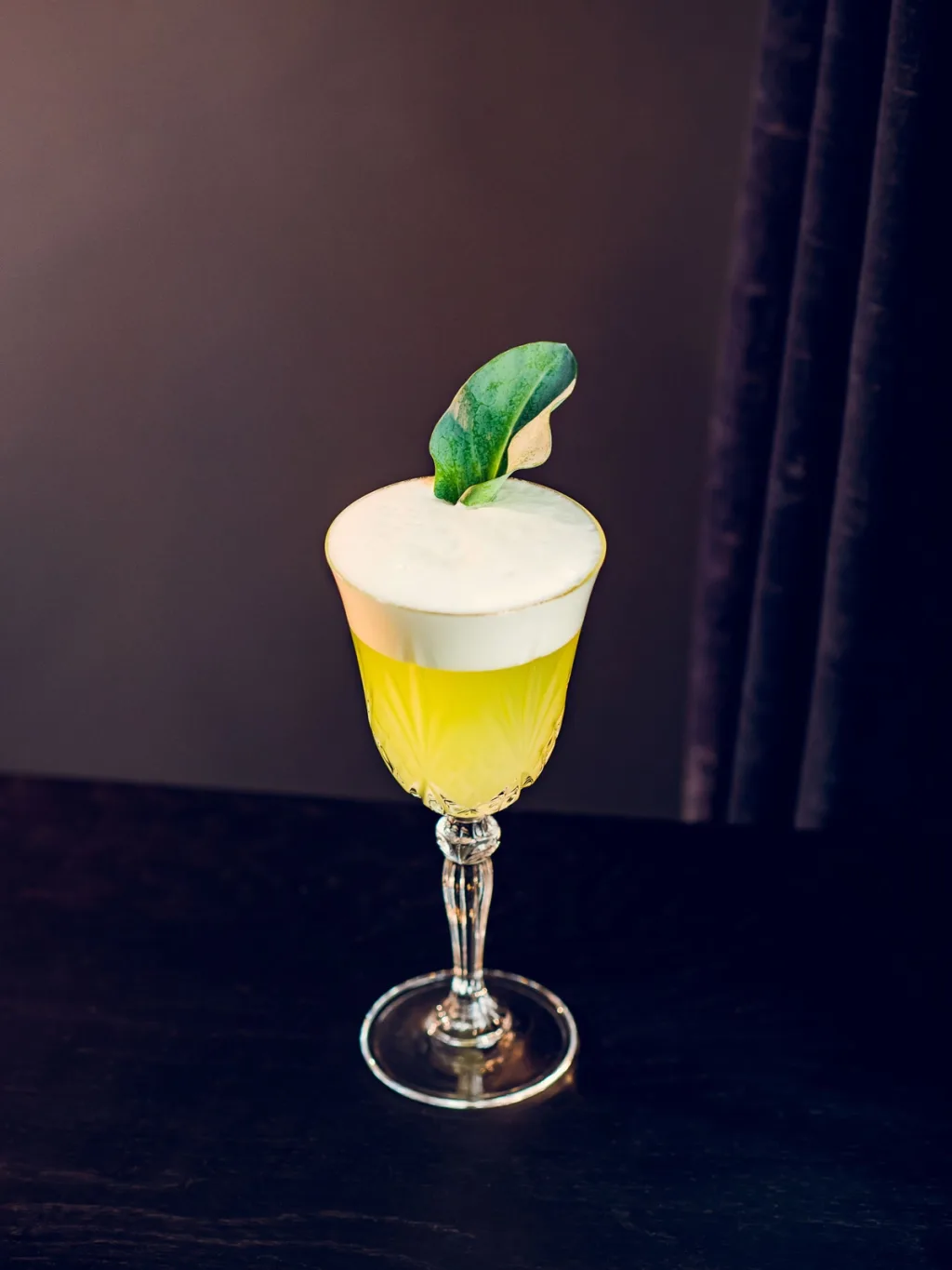 Yellow cocktail with white foam and a green leaf garnish for Cyril Lignac’s Saisons cookbook