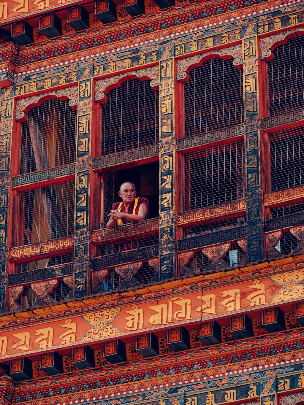 A monk at a window of an ornately carved Bhutanese temple, photographed for Six Senses Bhutan hotel