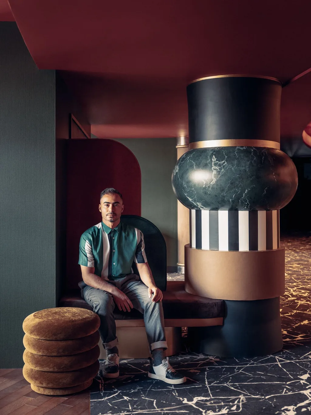 Man seated beside a striped marble column and stacked velvet pouf, Nest MGallery Hotel, Paris