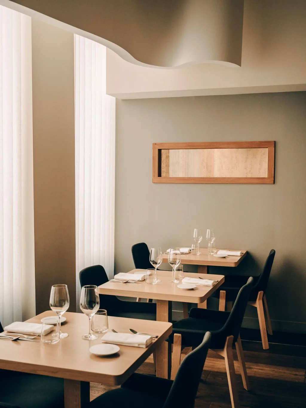 Pale wooden tables with dark chairs beside sheer curtains in a Lyon restaurant