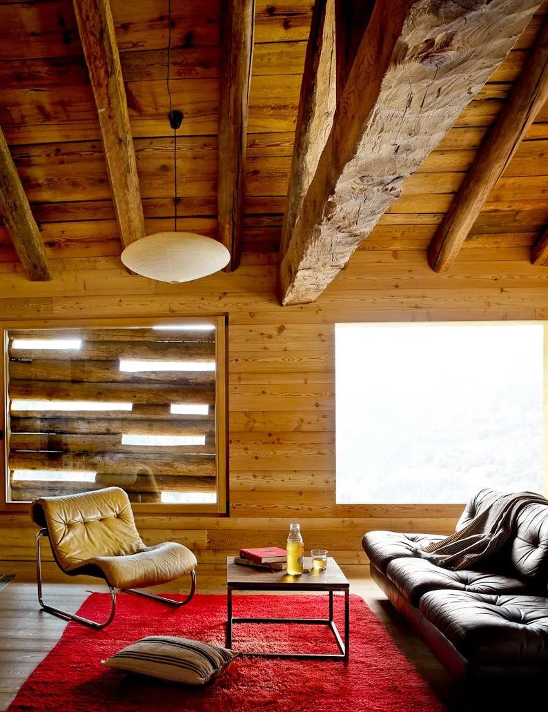 Living room with a log-slat window, leather chairs, and a red rug at Montagne Alternative hotel, Switzerland