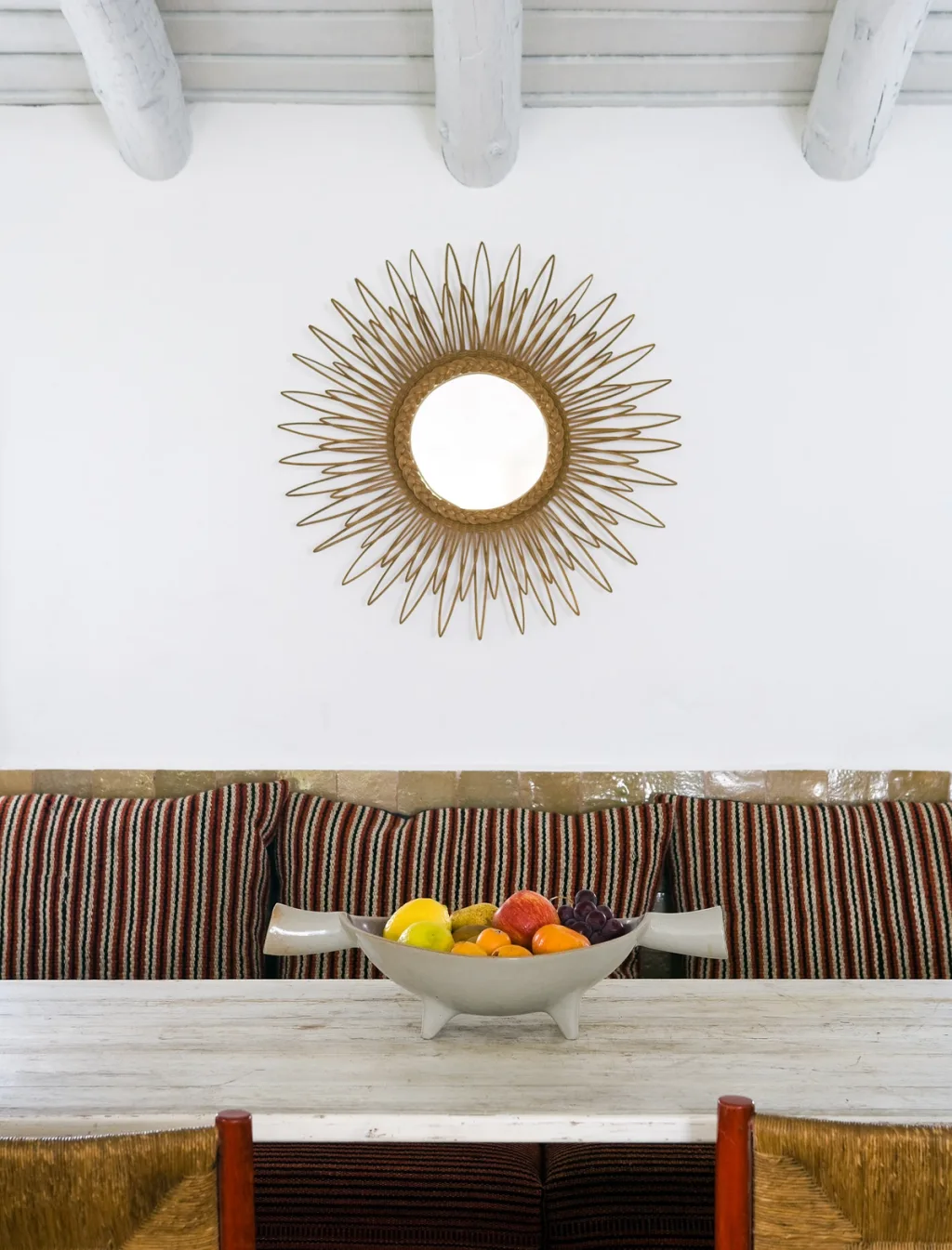 Sunburst mirror above a striped dining bench and bowl of fruit, Jacques Grange, Comporta