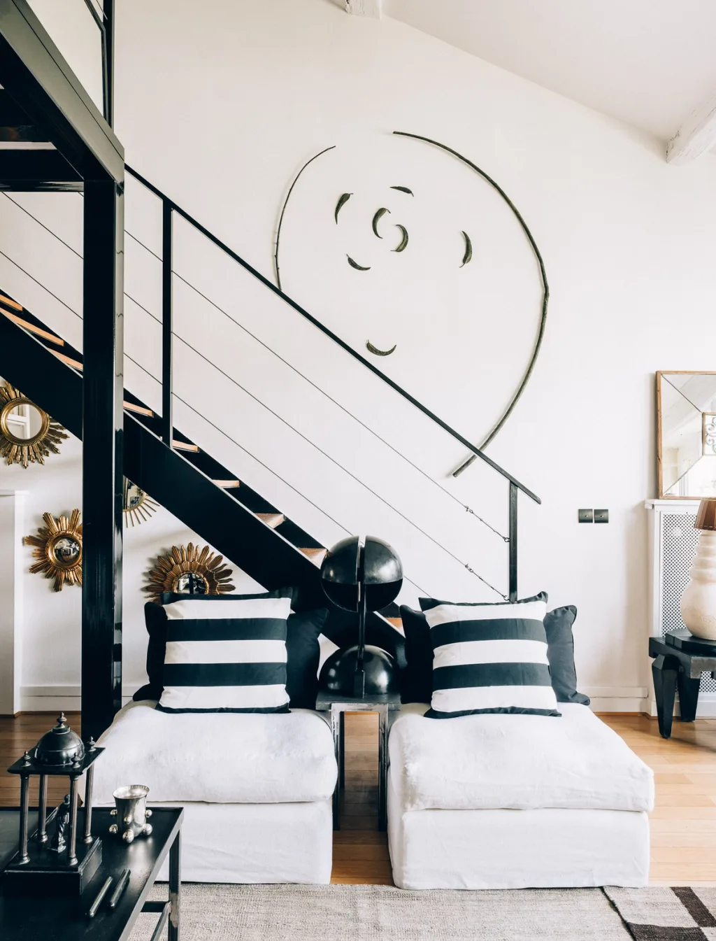 Two white lounge chairs with striped cushions beneath a black staircase, Michel Klein, Paris