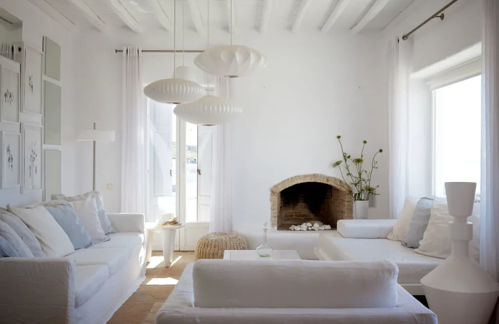 All-white living room with three oval paper pendant lamps and a stone fireplace, a hotel in Mykonos