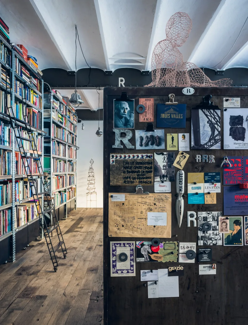 Tall library shelves beside a collage-covered partition at Daniel Rozensztroch's Paris home