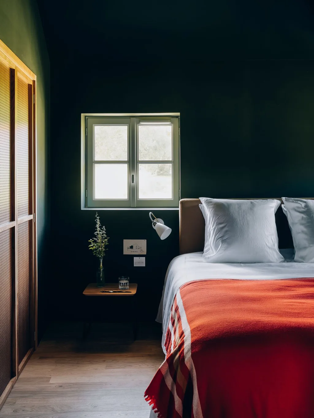 Dark green bedroom with a red striped throw and a small garden window, Le Barn hotel