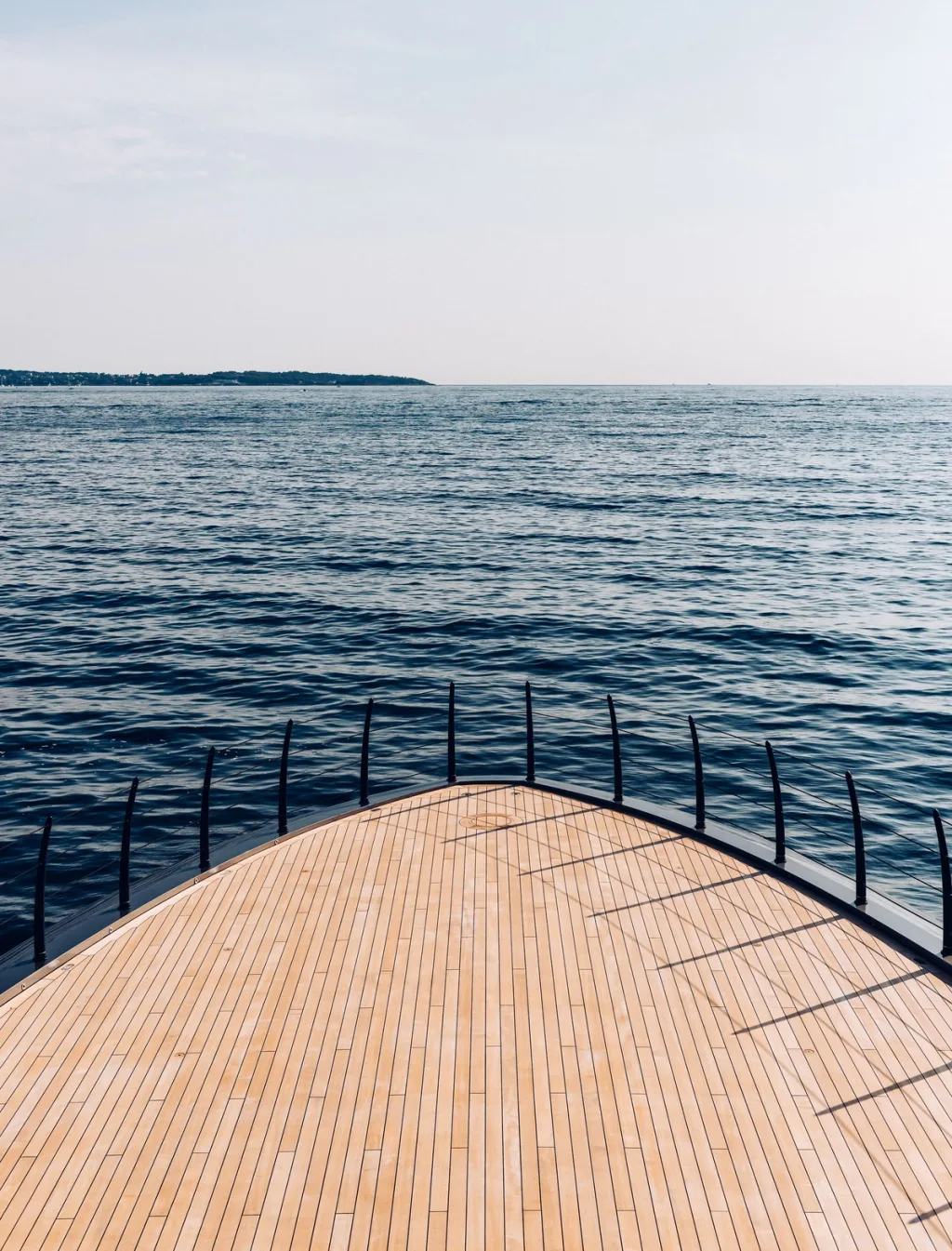 Curved wooden foredeck and slender black railings facing open water aboard Atlante