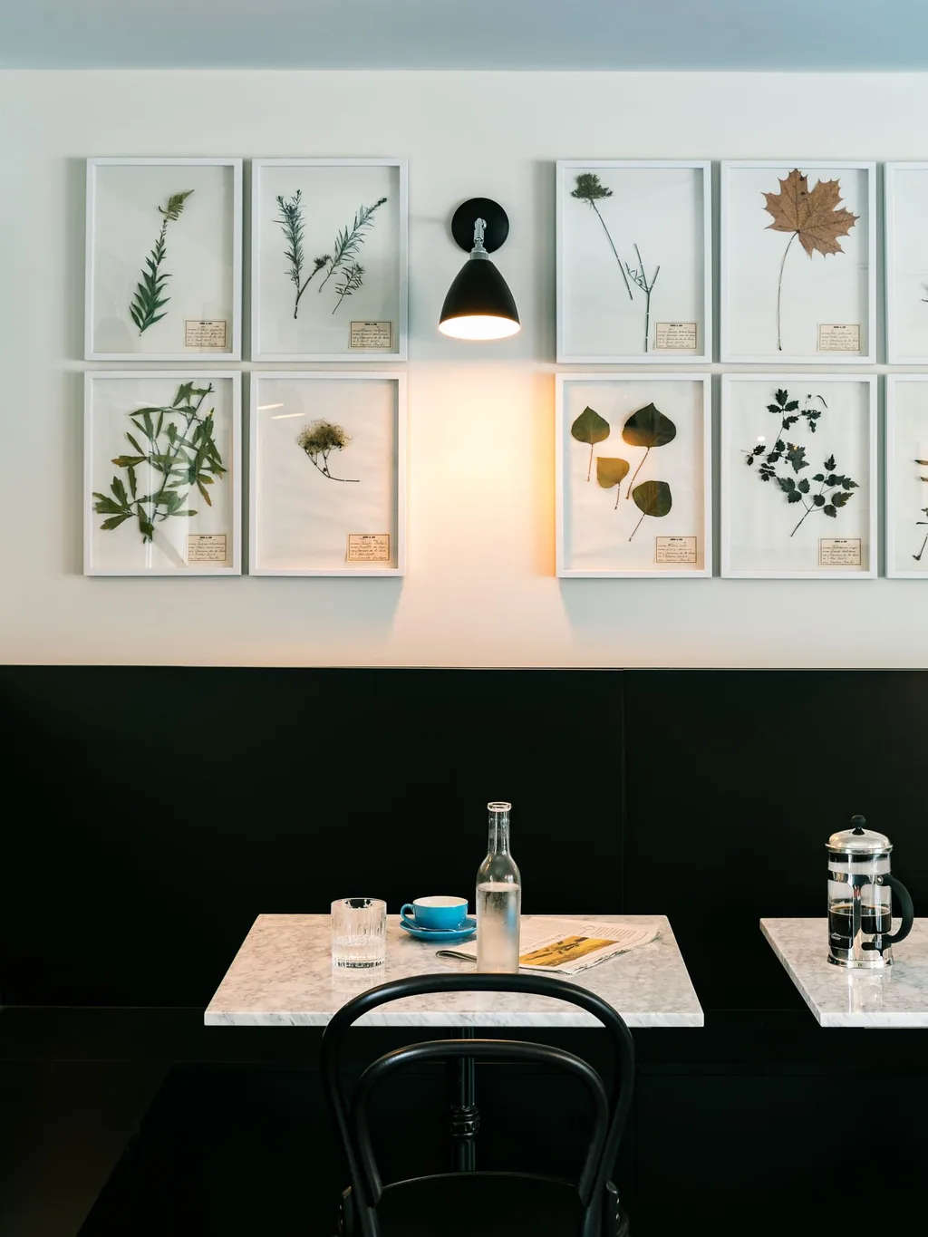Framed pressed botanical specimens above a cafe table set for coffee, Le Barn hotel