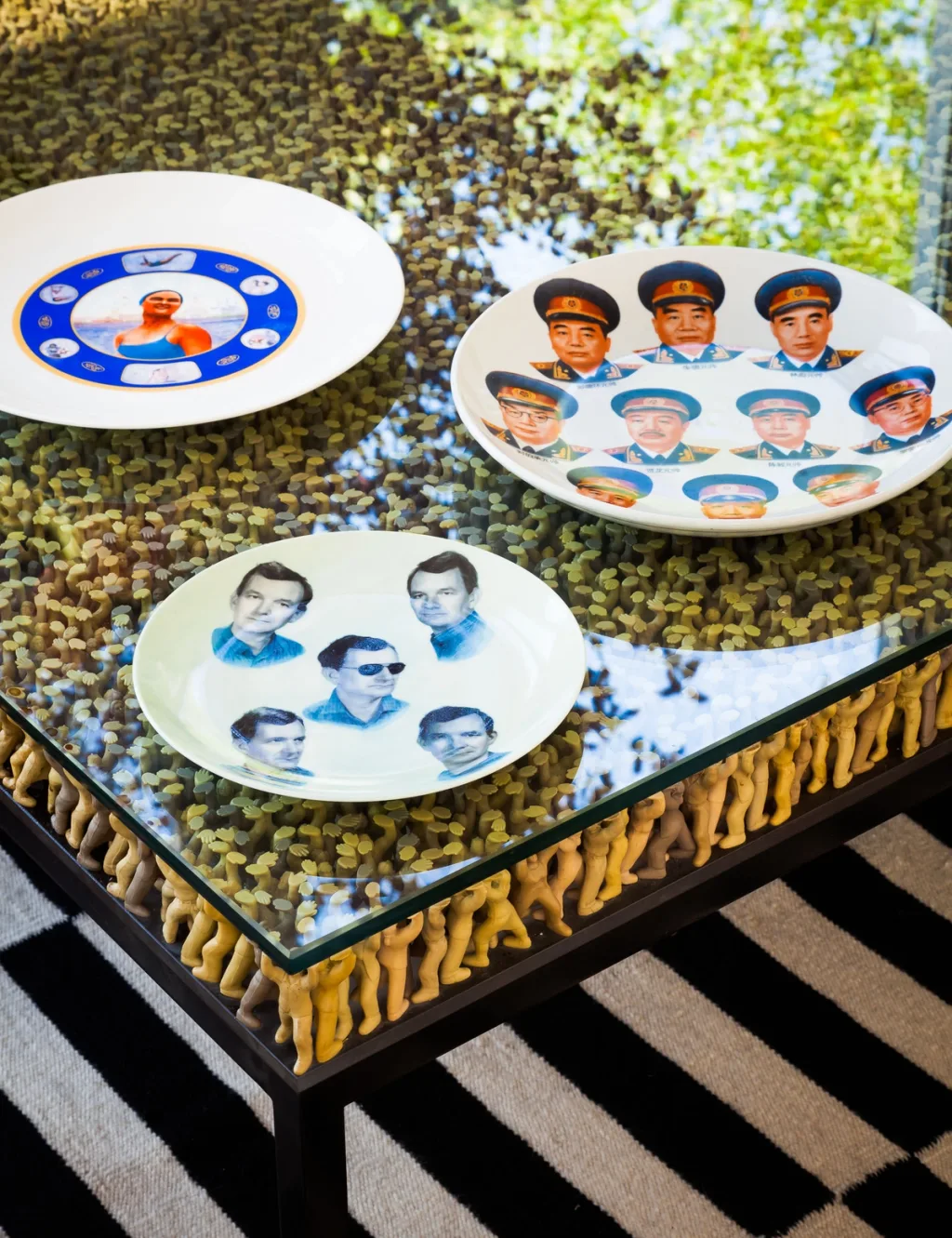 Three portrait-decorated plates on a glass-topped table of tiny figures, Suzanne Slesin, New York