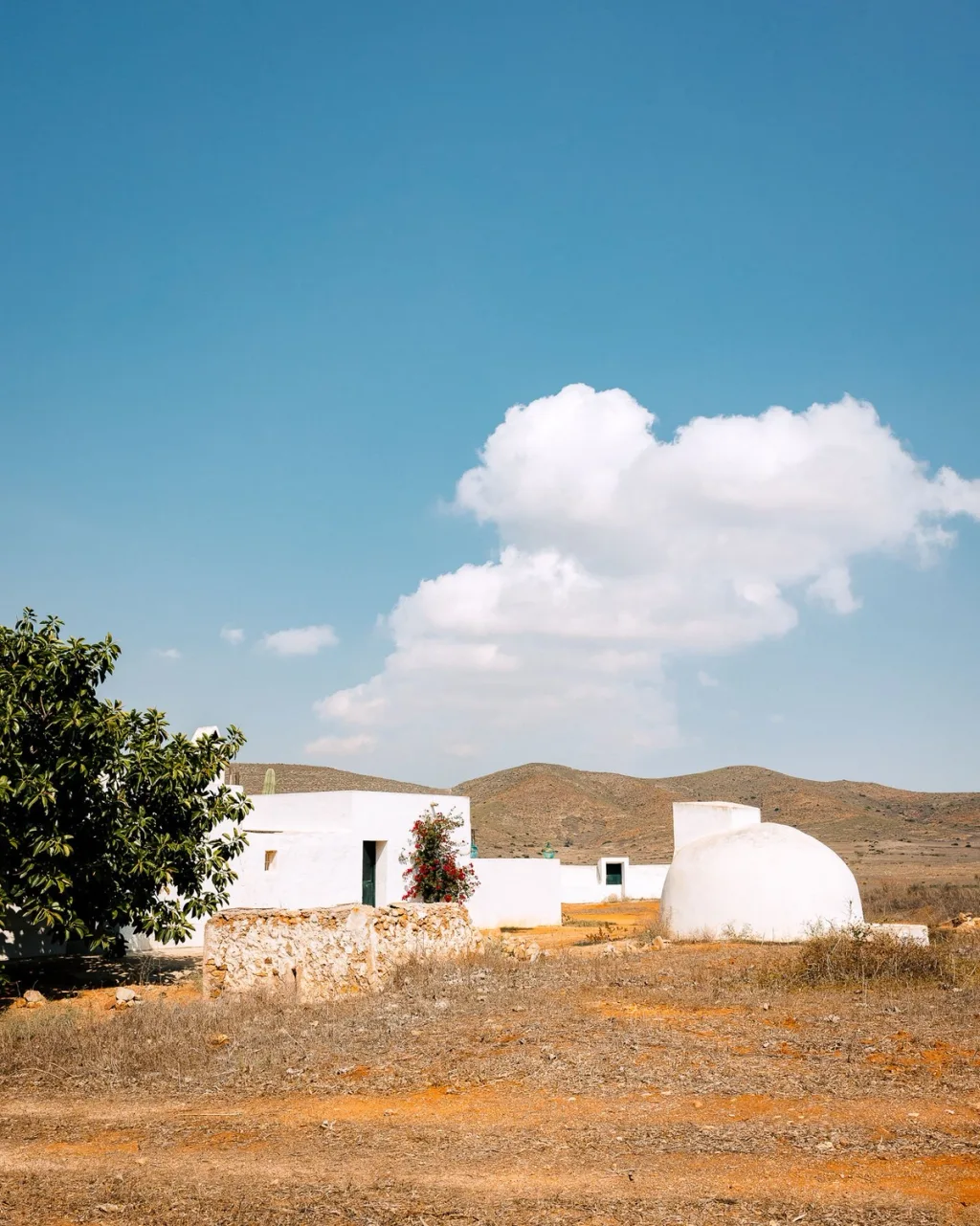 Low white buildings and a rounded structure in a dry landscape beneath blue sky in Almeria