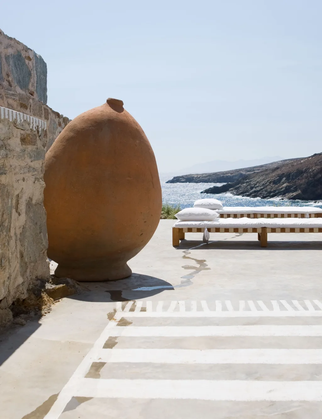 Large terracotta vessel beside white-cushioned sunbeds facing the sea, Paola Navone, Serifos