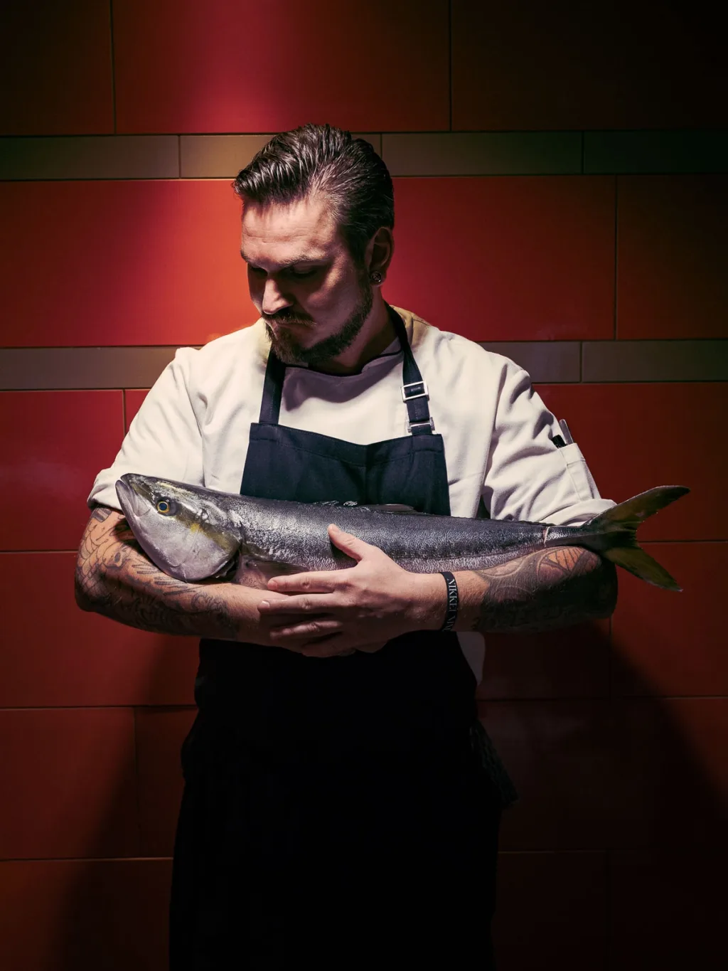 Apron-clad chef holding a whole fish against a red wall at Fairmont Hotel, Hamburg