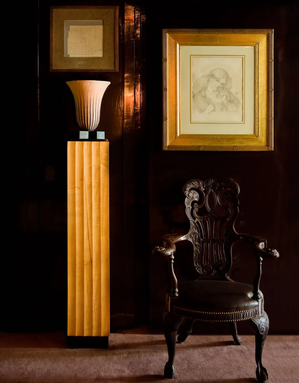 Carved dark armchair beneath framed drawings beside a tall pedestal, Yves Saint Laurent, Paris