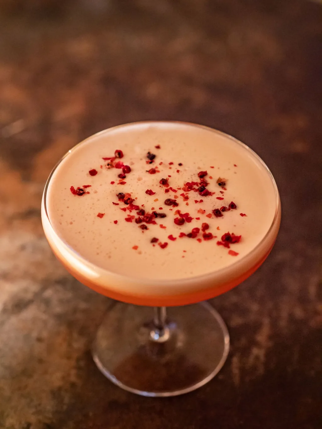 Pink foamy cocktail with a red garnish in a coupe for Cyril Lignac’s Saisons cookbook