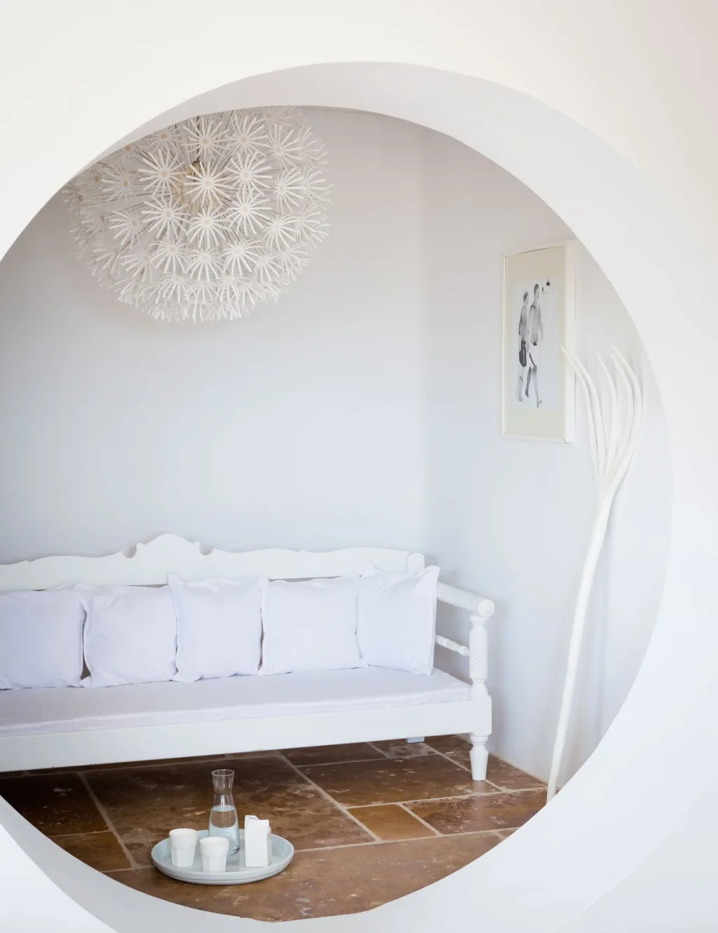 Circular wall opening frames a white daybed and breakfast tray, a hotel in Mykonos
