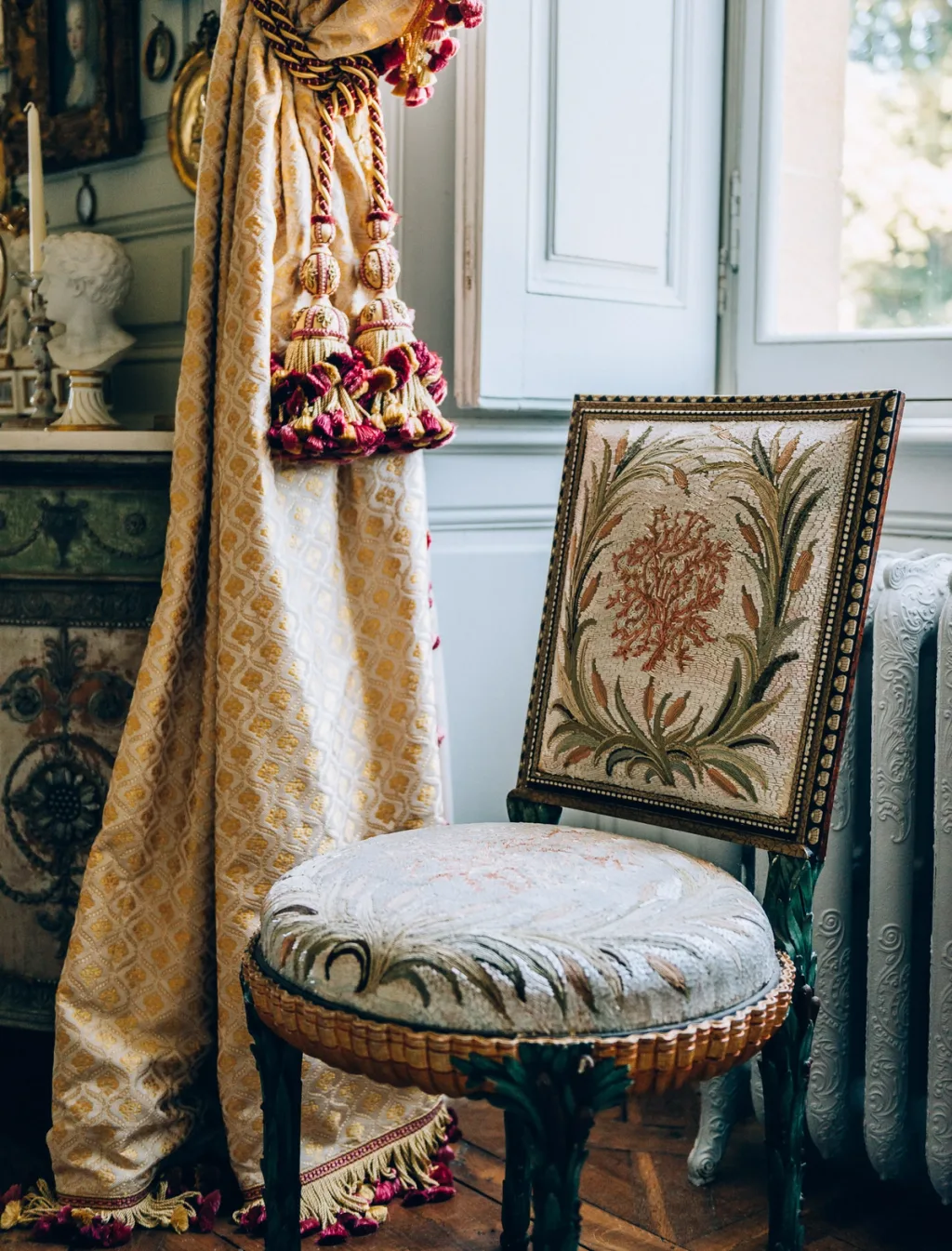 Embroidered chair beside a tasseled gold curtain and tall window at Chateau de Digoine