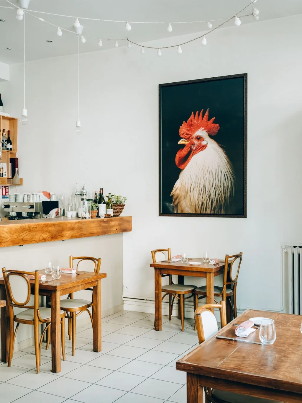 Wooden tables beneath a large rooster portrait and strings of bulbs in a Lyon restaurant