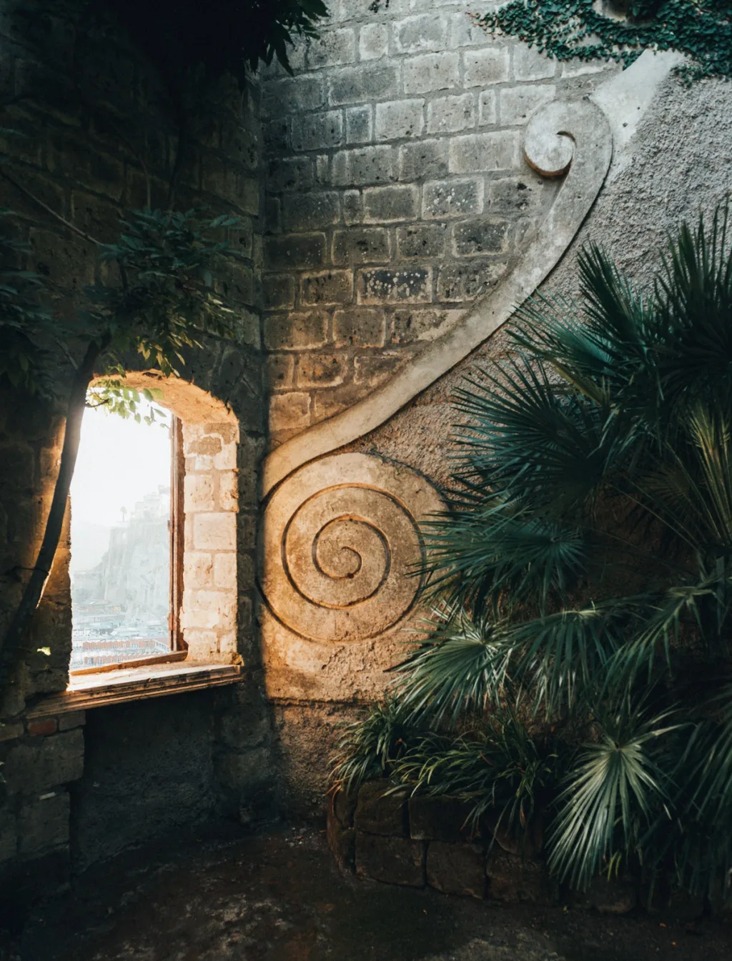 Large spiral stone ornament beside a bright opening and dense palms at Villa Astor