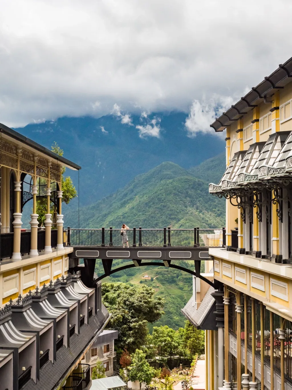 Guest crosses an arched skywalk linking two yellow colonial buildings, Hotel de la Coupole MGallery, Sapa, Vietnam