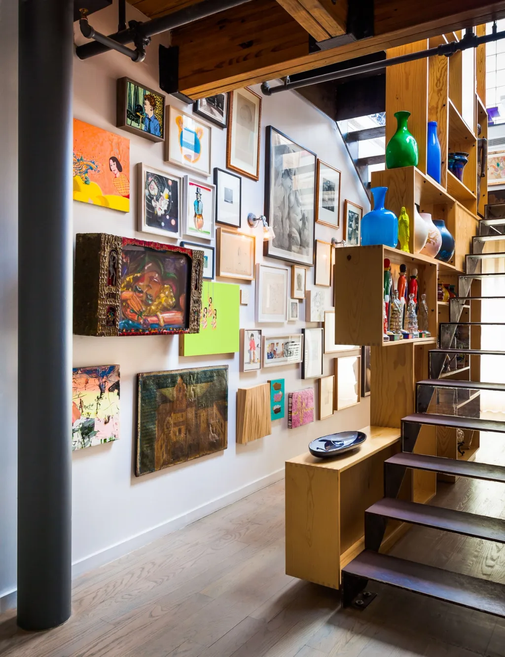 Art-covered wall beside a staircase and shelves of colourful vases, Suzanne Slesin, New York
