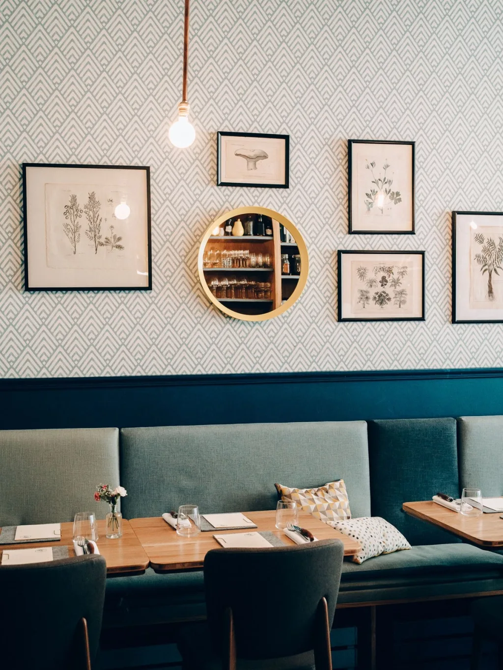 Green banquette beneath botanical drawings and a round mirror in a Lyon restaurant