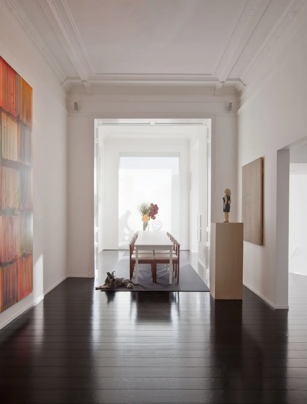 White rooms aligned toward a bright dining table across dark floors in the James Van Damme series