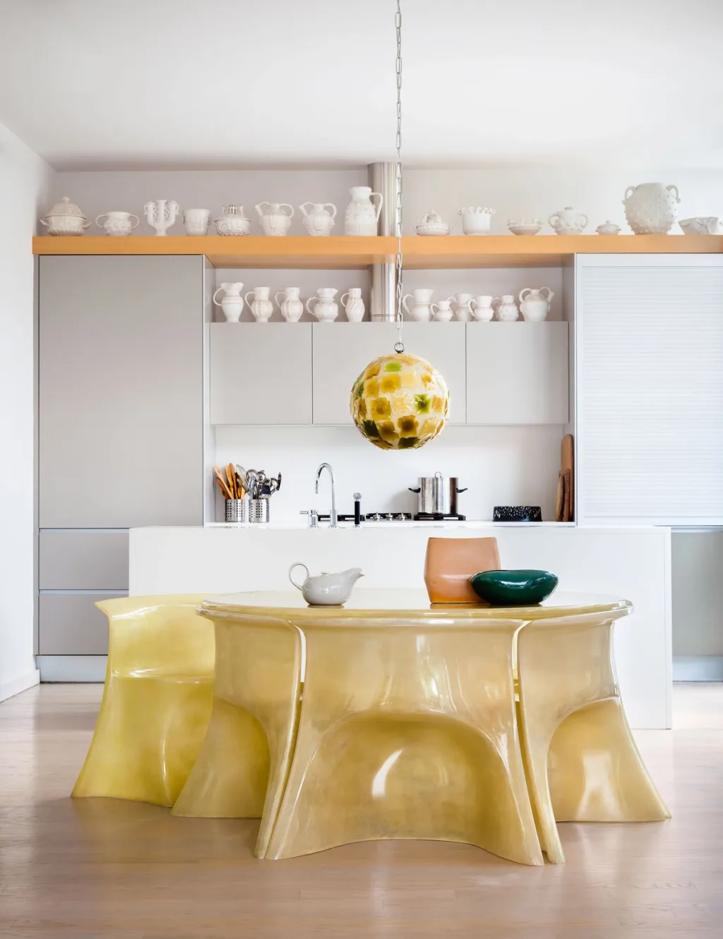 Sculptural yellow dining furniture before a kitchen lined with white vessels, Suzanne Slesin, New York