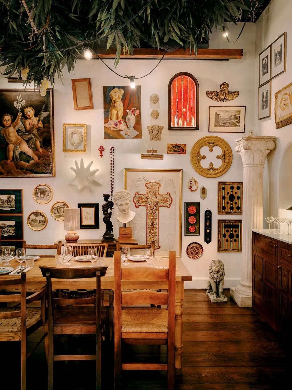 Wooden dining chairs beneath a wall of framed art and sculptural objects at Big Mamma, UK