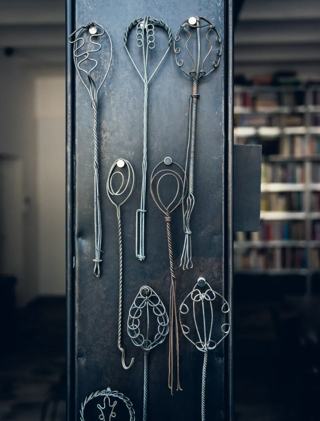 Collection of looped wire utensils displayed on a dark panel at Daniel Rozensztroch's Paris home