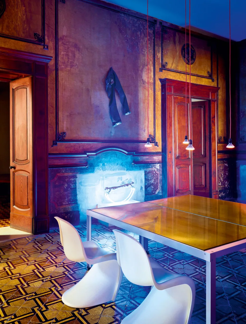 White dining chairs around a reflective table in the richly coloured Antonio G. Martiniello interior, Naples