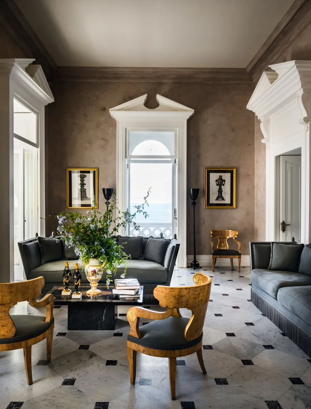 Grey sofas and golden wooden chairs beneath ornate window surrounds at Villa Astor