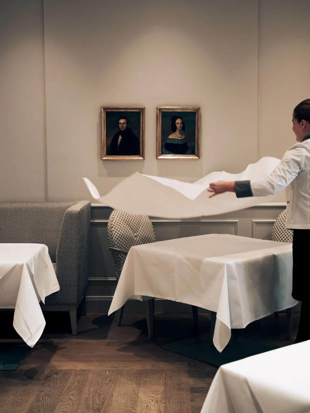 Staff member spreading a white tablecloth beneath framed portraits at Fairmont Hotel, Hamburg