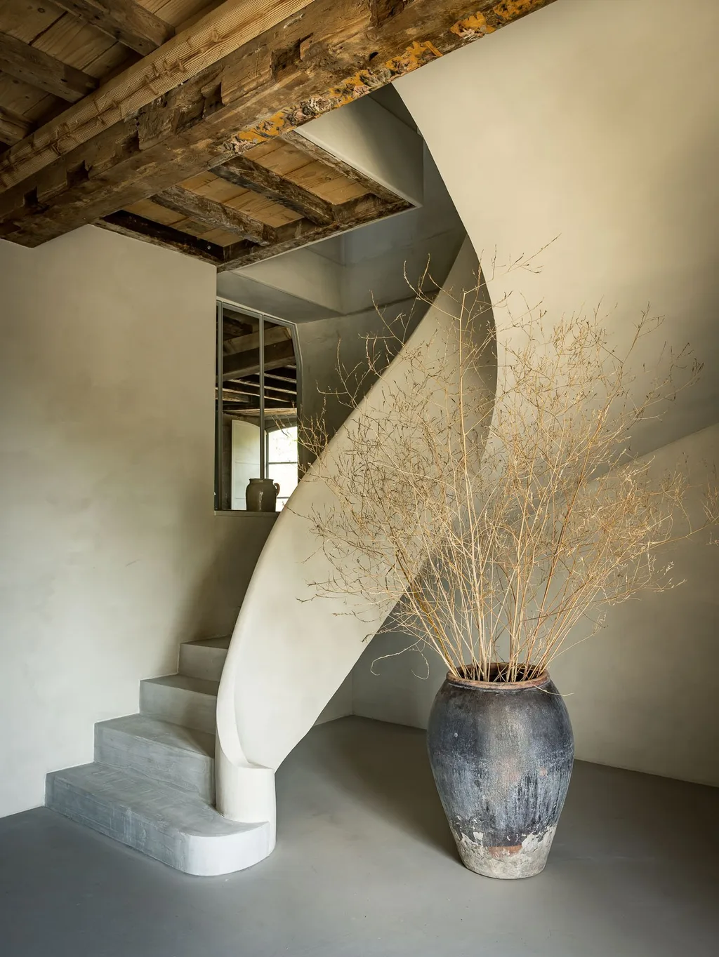 Curved plaster staircase holds a weathered urn with dried branches, Manufacture Royale de Lectoure hotel