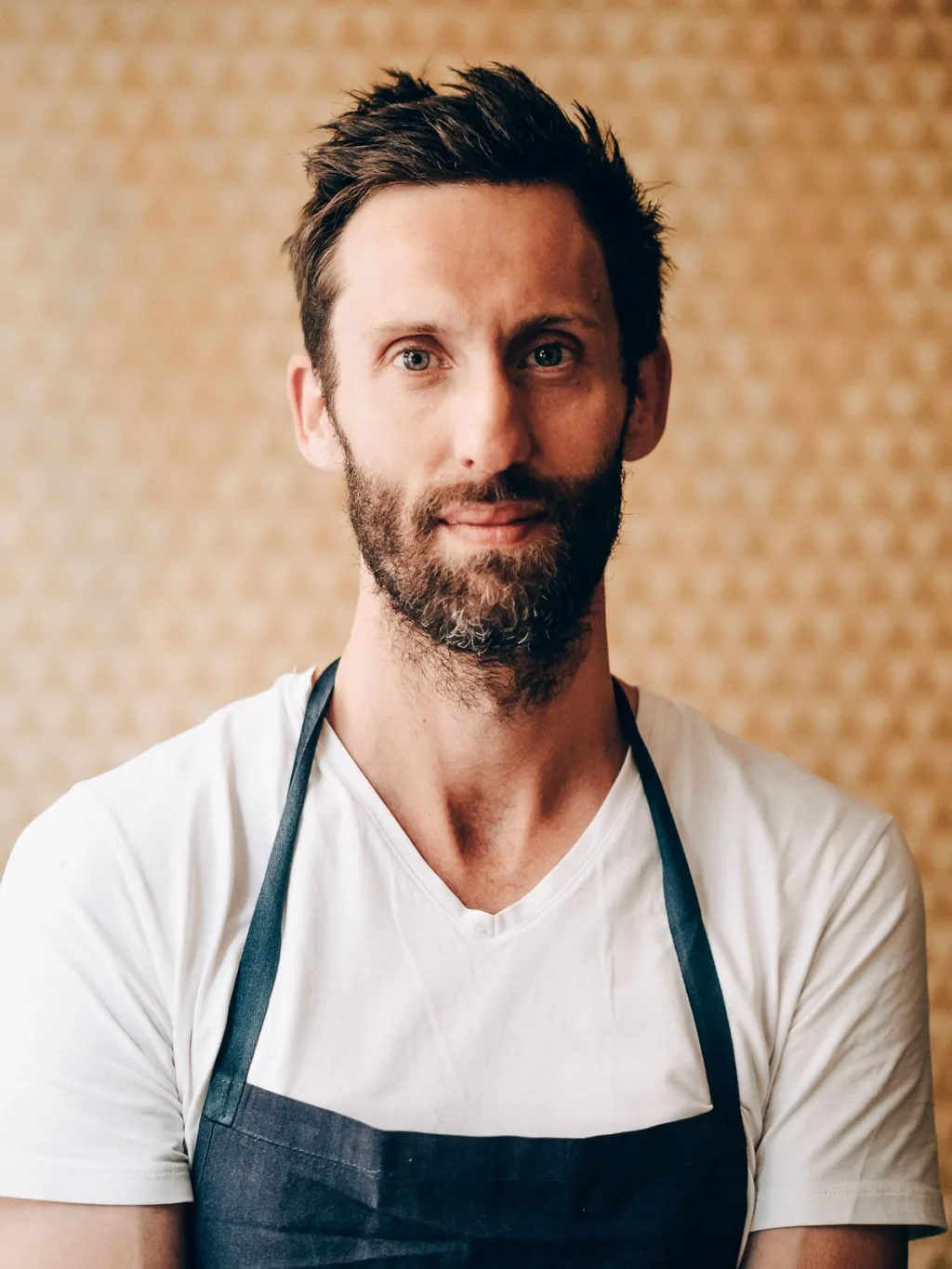 Portrait of a bearded man in a white T-shirt and dark apron for the Lyon restaurant series